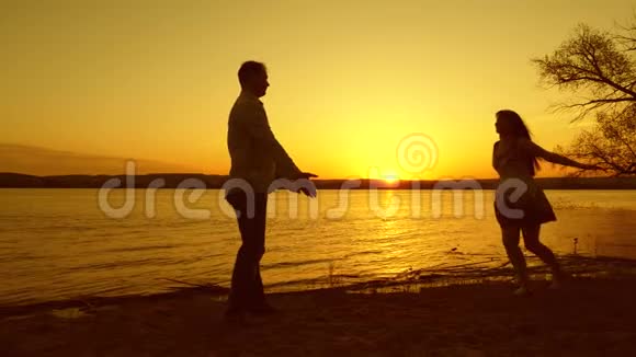 爱上一个女孩和男人晚上在沙滩上跳舞在黄色的夕阳下视频的预览图