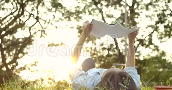 日落时分年轻迷人的亚洲女人躺在公园的绿草上看书视频的预览图
