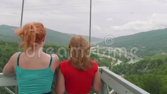 两个年轻的女人在山上看着绿色的山谷在电车上看着游客视频的预览图