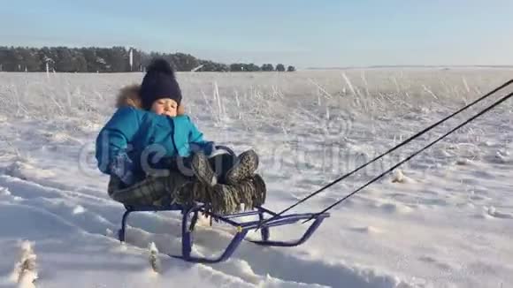 坐雪橇的小男孩宝贝在雪橇上孩子们在雪地里户外玩耍愉快的寒假冬季视频的预览图