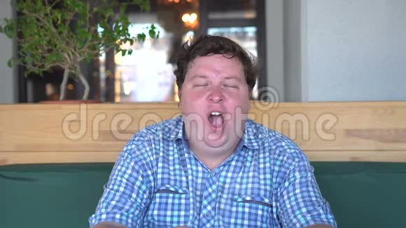 在咖啡馆或餐馆打哈欠的疲惫胖子的画像视频的预览图