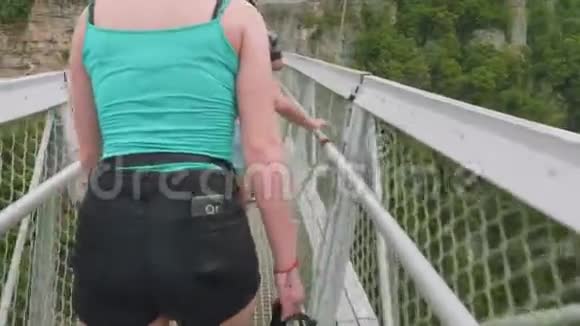 两位年轻女子在青山谷和山河上的大悬索桥上行走的后景视频的预览图
