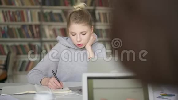 金发的年轻女学生在图书馆的笔记本上写作视频的预览图