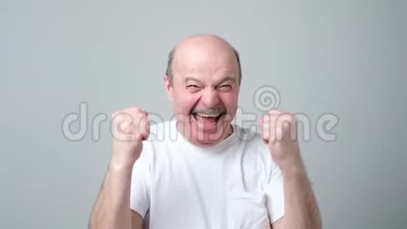 快乐的秃头老人在灰色背景下庆祝他的成功视频的预览图