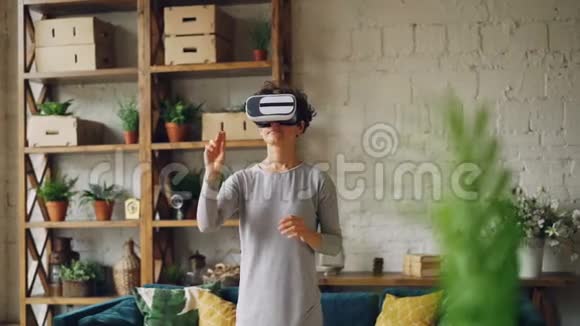 苗条的女孩正在家中使用虚拟现实眼镜站在阁楼风格的房间里手在玩游戏现代视频的预览图
