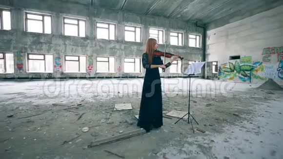 红发女士正在一座搁浅的大楼里拉小提琴视频的预览图
