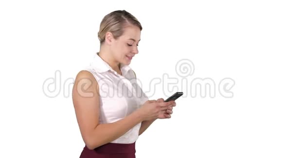 给朋友发短信漂亮的年轻女人拿着智能手机站在白色的地上微笑着看着它视频的预览图