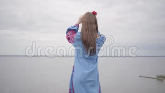后景在无忧无虑的白种人女人穿着夏日的长时装站在田野的背景上视频的预览图