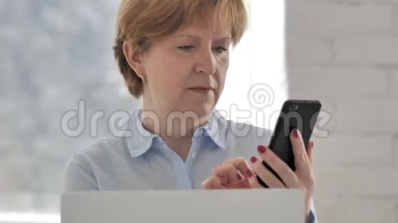 老女人在电话上说话在笔记本电脑上工作视频的预览图