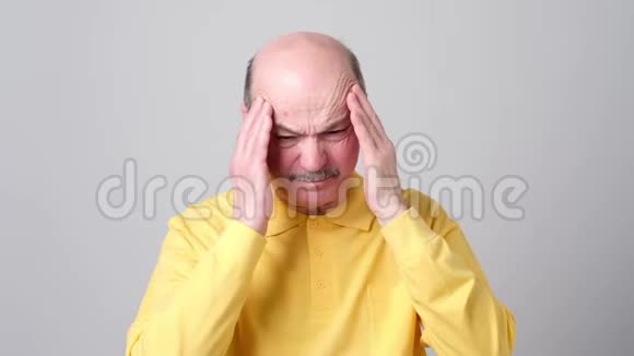 成熟的男人穿着黄色的t恤闭着眼睛痛苦地摸着他的头视频的预览图