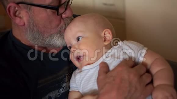 爷爷抱着一个小孙子一个留着灰色胡子的老人和一岁的小男孩视频的预览图