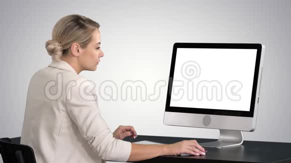 年轻女性在办公室工作坐在办公桌前在梯度背景上看监视器视频的预览图