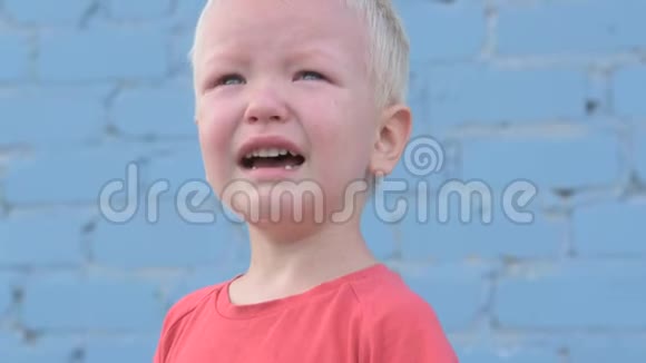 穿着红色T恤的金发小男孩在灰色砖墙上泪流满面视频的预览图
