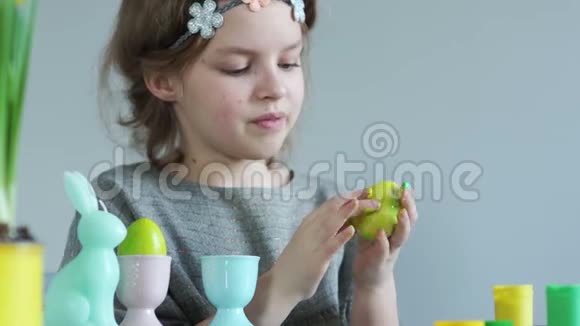女孩用手指画复活节彩蛋艺术治疗戴着花圈的可爱女学生手里拿着浅绿色视频的预览图