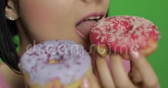 快乐美丽的女孩摆姿势舔着五颜六色的甜甜甜圈视频的预览图