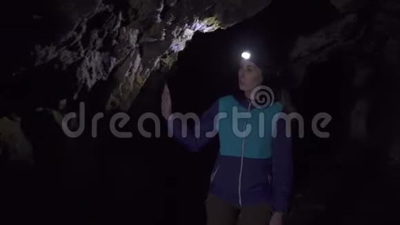 肖像女旅行者带着一个背包去洞穴额头上戴着手电筒检查着石头视频的预览图