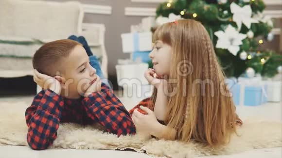 可爱的孩子们在一起度过愉快的时光在圣诞树附近的地毯上交流视频的预览图
