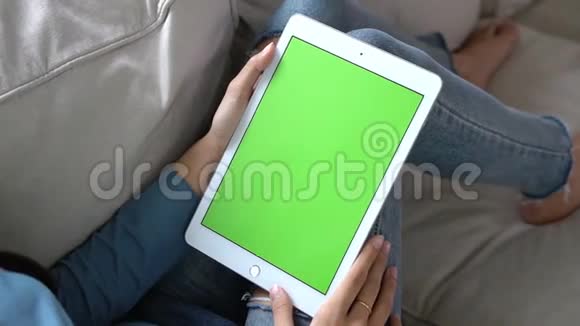 亚洲女人手牵着手用绿色屏幕的平板电脑观看自己在沙发上的定制内容视频的预览图