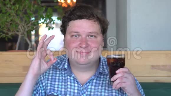 胖子拿着一杯饮料可乐在咖啡馆里并表现出良好的姿态相机视频的预览图