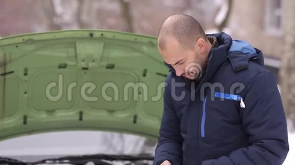 下雪的冬天一个男人在一辆破车的背景上用一个敞篷的引擎盖称为拖车视频的预览图