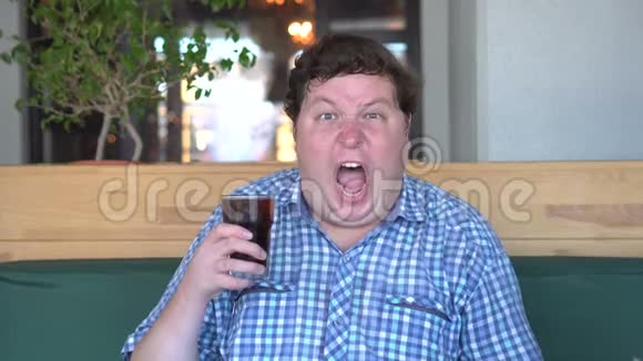 惊慌失措的胖子拿着一杯饮料可乐愤怒地尖叫坐在咖啡馆里饮料视频的预览图