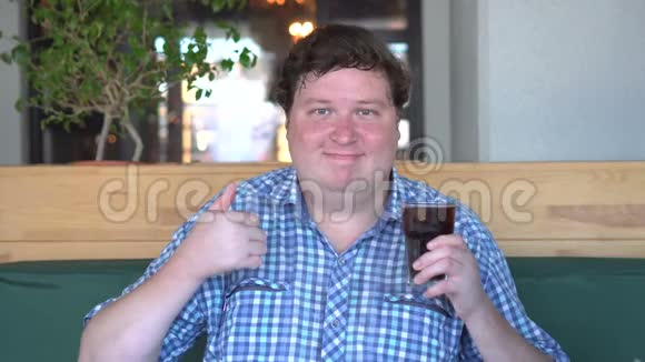胖胖的快乐男人拿着一杯饮料可乐站在咖啡馆里伸出大拇指饮料视频的预览图