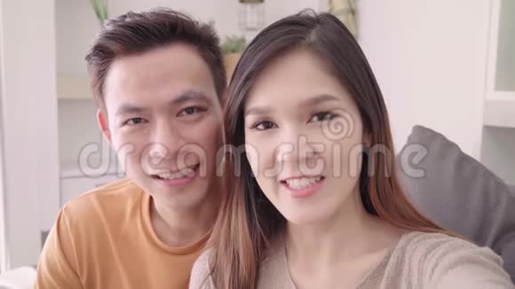 亚洲夫妇使用智能手机视频电话与朋友在家客厅甜蜜的夫妇享受爱情的时刻视频的预览图