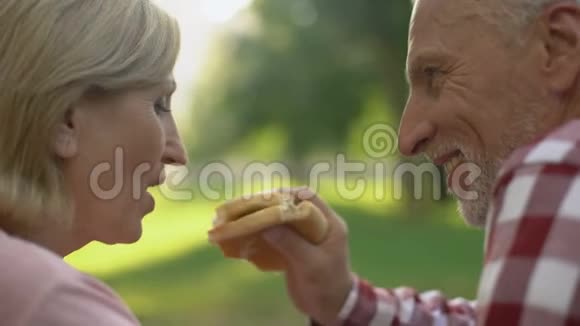 美丽的皱纹女人在野餐时喂丈夫快餐汉堡约会视频的预览图