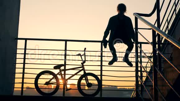 日落时分年轻人正从栏杆上跳下来骑着自行车离开视频的预览图