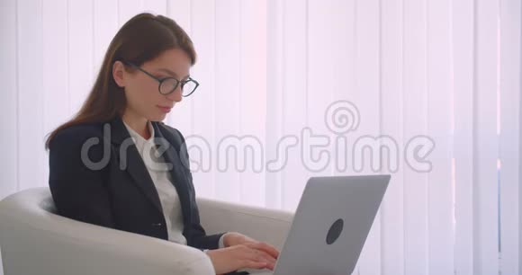特写侧景照片年轻的高加索女商人戴着眼镜用笔记本电脑看着镜头微笑视频的预览图