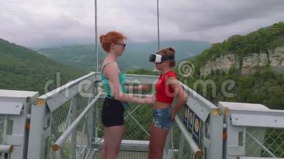 红发白种人的姐姐从年轻的金发女郎身上摘下虚拟现实眼镜对着山谷视频的预览图