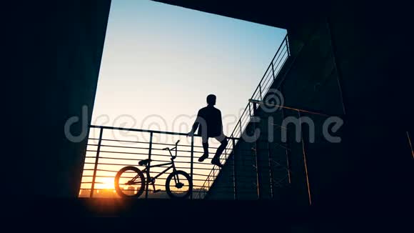 夕阳下一个骑自行车坐在栏杆上的年轻人的剪影视频的预览图