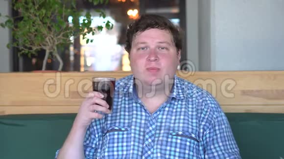 胖子拿着一杯饮料可乐坐在咖啡馆里咀嚼食物饮料视频的预览图