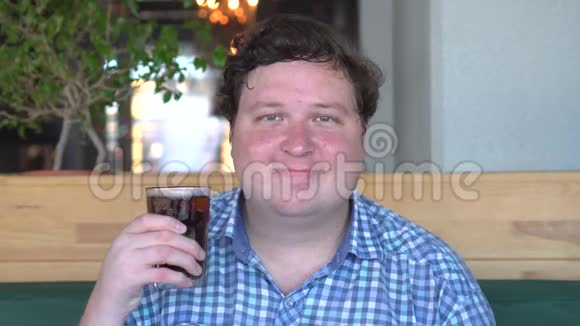 一幅胖子的画像他拿着一杯饮料可乐坐在咖啡馆里对着镜头微笑视频的预览图
