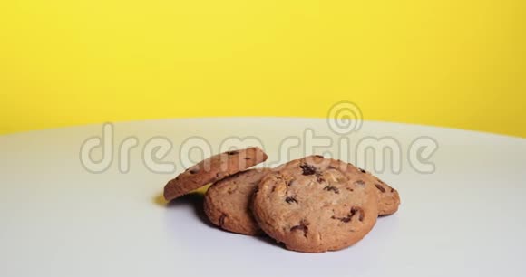 带有巧克力片和葡萄干的美式饼干在黄色背景的白色桌子上旋转职业介绍所视频的预览图