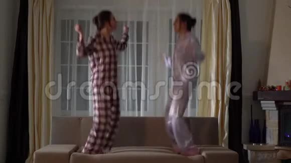 两个快乐的双胞胎姐妹在一个舒适的客厅里跳在沙发上像在童年一样快乐视频的预览图