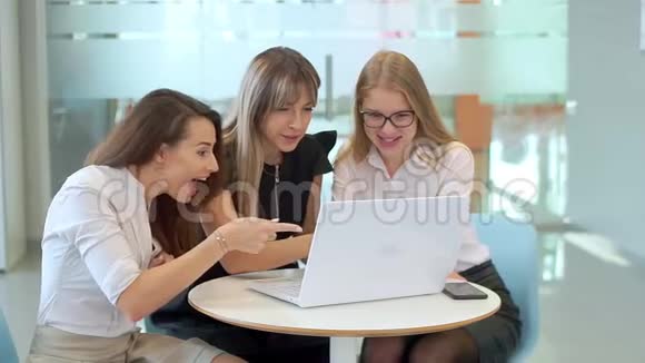 办公室里的女孩们看着笔记本电脑开始享受关于她们工作成就的好消息视频的预览图