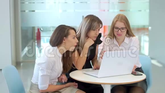 办公室里的女孩们看着笔记本电脑开始享受关于她们工作成就的好消息视频的预览图