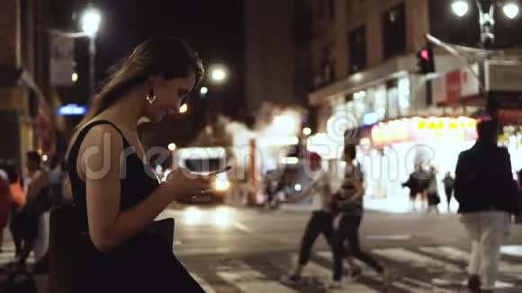 年轻快乐的女人站在拥挤的市中心靠近美国纽约的交通道路使用智能手机视频的预览图