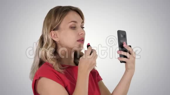 金发女人涂着口红在渐变背景下看着手机视频的预览图