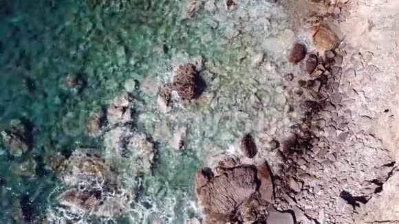 从上到下在岩石海岸看到晶莹剔透的海浪清澈的蓝色海水沿着海岸线飞行视频的预览图