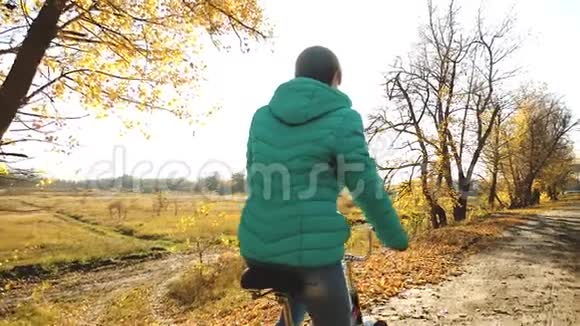 女孩在阳光明媚的秋叶上骑自行车视频的预览图