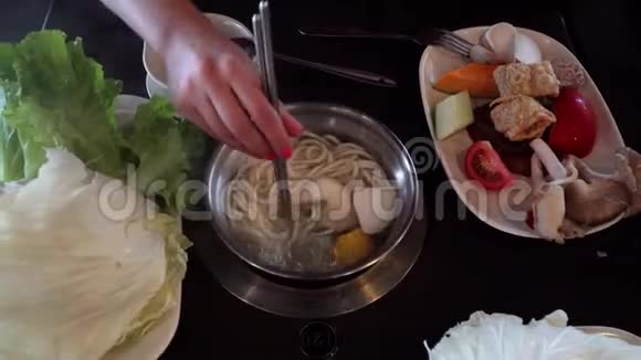 手把蔬菜和肉放进火锅里在中餐厅吃饭顶部视图视频的预览图
