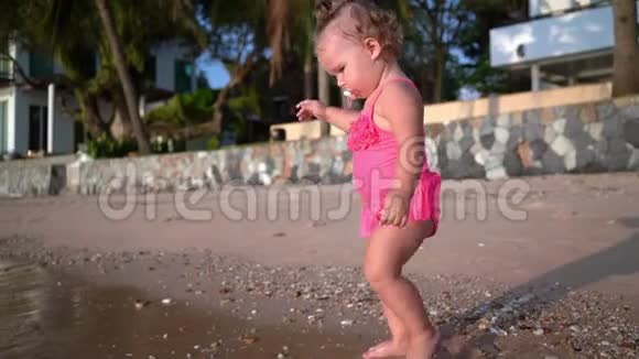 日落时分穿着粉红色泳衣的可爱小女孩沿着海滨散步慢动作视频的预览图