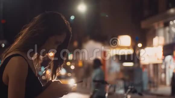 年轻快乐的女人晚上站在拥挤的市中心和使用智能手机在纽约美国视频的预览图