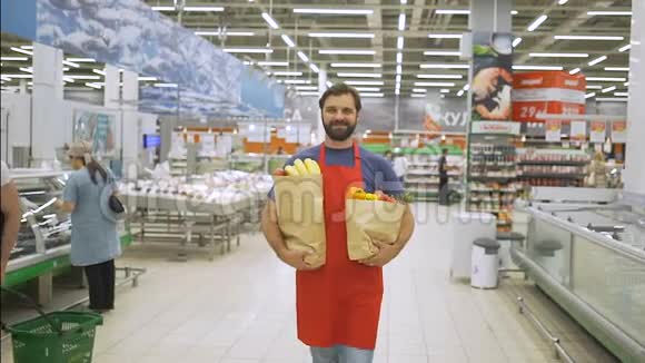 英俊的商店职员站在超市里拿着购物袋他正对着照相机微笑视频的预览图