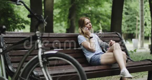 一位年轻的女运动员正在公园里的长凳上休息用她的手机说话视频的预览图