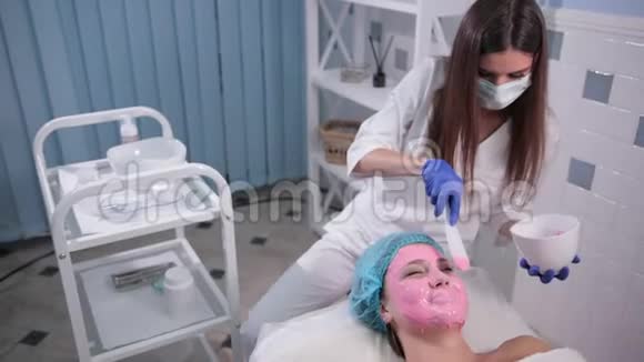 护士医生给女性做面部按摩用刷子做粉色面膜视频的预览图