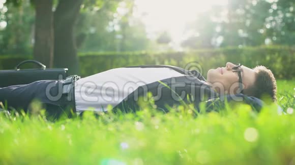 快乐的人穿着西装躺在草地上享受阳光明媚的日子与自然和谐相处视频的预览图