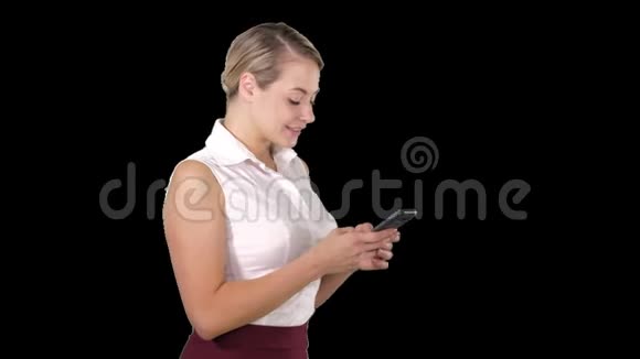 发短信给有魅力的年轻女性她拿着智能手机站着微笑着看着它阿尔法频道视频的预览图